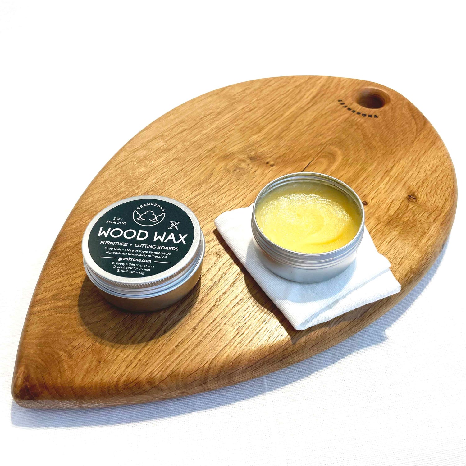Wood wax by Grankrona on top of a shiny cutting board with a cloth to spread it