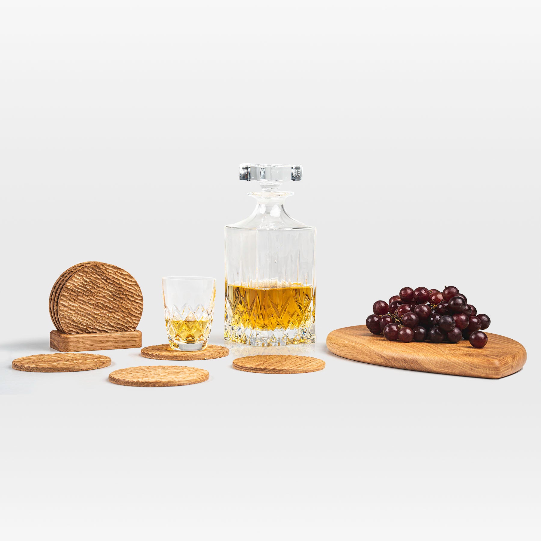 'Bark' coaster set with a glass and bottle of whiskey next to a serving board with grapes